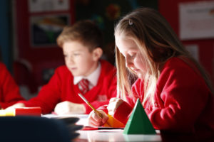 Two young pupils are seen focusing on their work with pencils in their hands.