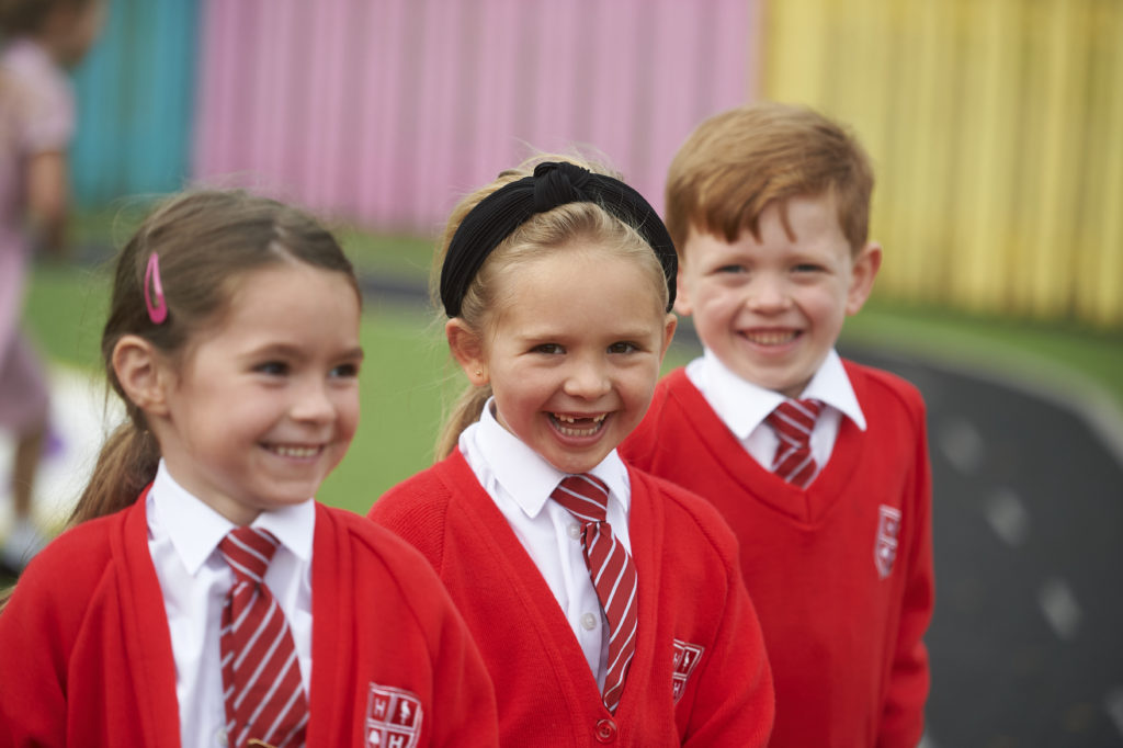 Three pupils are seen smiling for the camera in their red High Halstow school uniform.