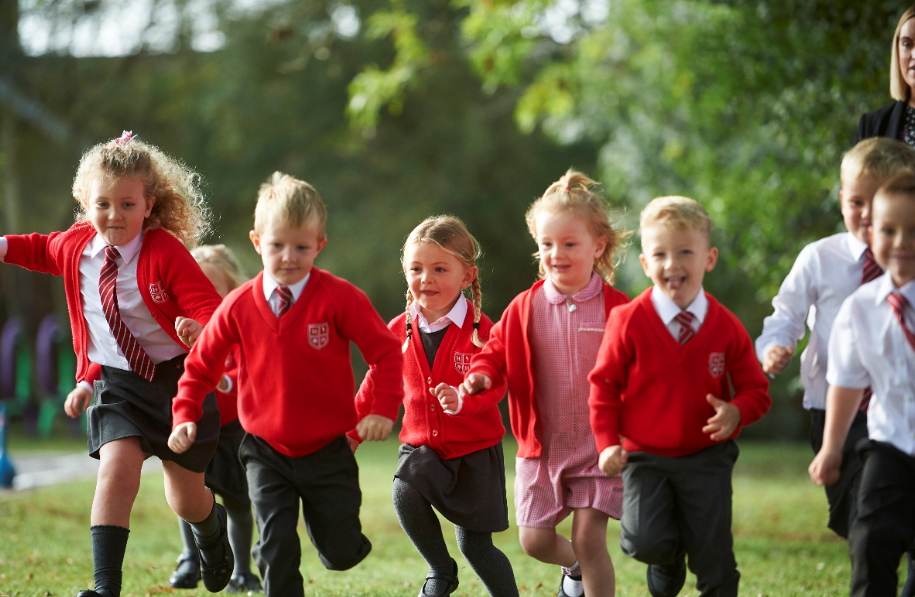 A group of pupils can be seen running across a field, wearing their High Halstow Primary Academy uniform.
