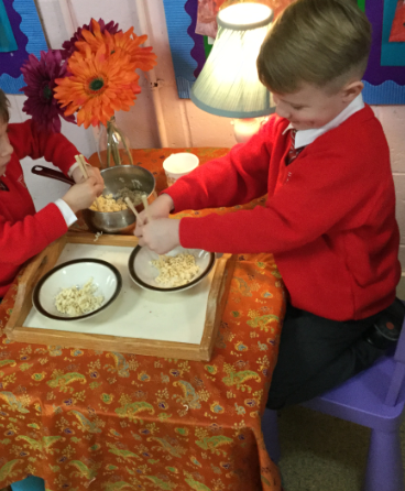 Two pupils are shown sitting down at a dinner table, eating Noodles with chopsticks.