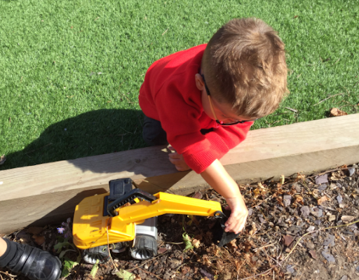 A young boy can be seen playing with a toy construction vehicle in an outdoor play area.
