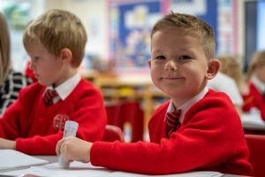 A young boy smiling at the camera in a classroom