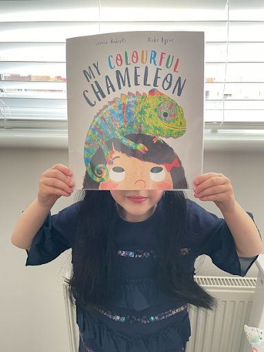 A pupil is seen posing for the camera with the picture book 'My Colourful Chameleon'.