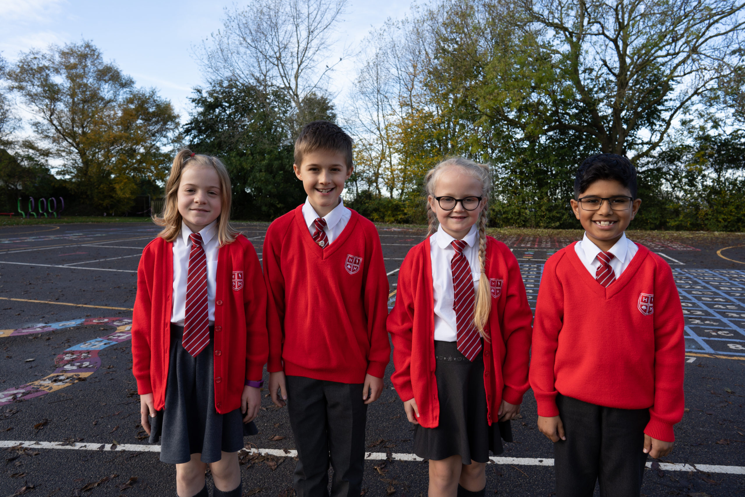 Four young pupils, two boys and two girls, are pictured standing alongside one another on the academy grounds. They are dressed in their academy uniform and smiling for the camera.
