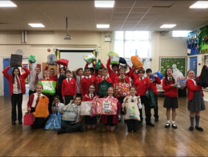 Year 6 pupils are seen standing together for a group photo, holding the bags they have filled with blankets, gloves, etc. to give to the local charity Medway Street Angels.