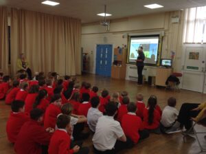 Children are seen sitting down together in the hall area, listening to a presentation being given to them by volunteers about different careers for Careers Week in March 2023.